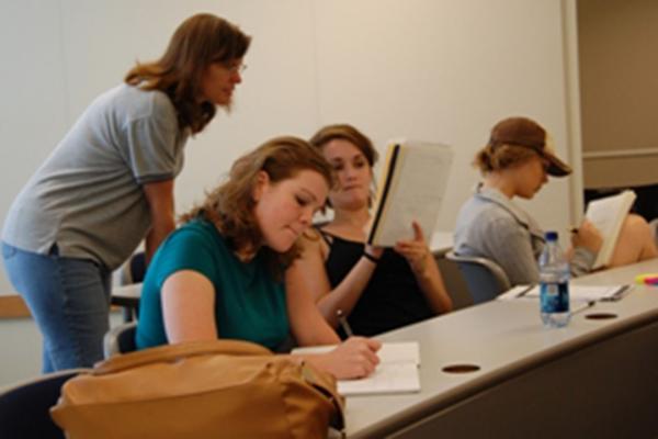 Three students working on math problems at a desk while an instructor assists